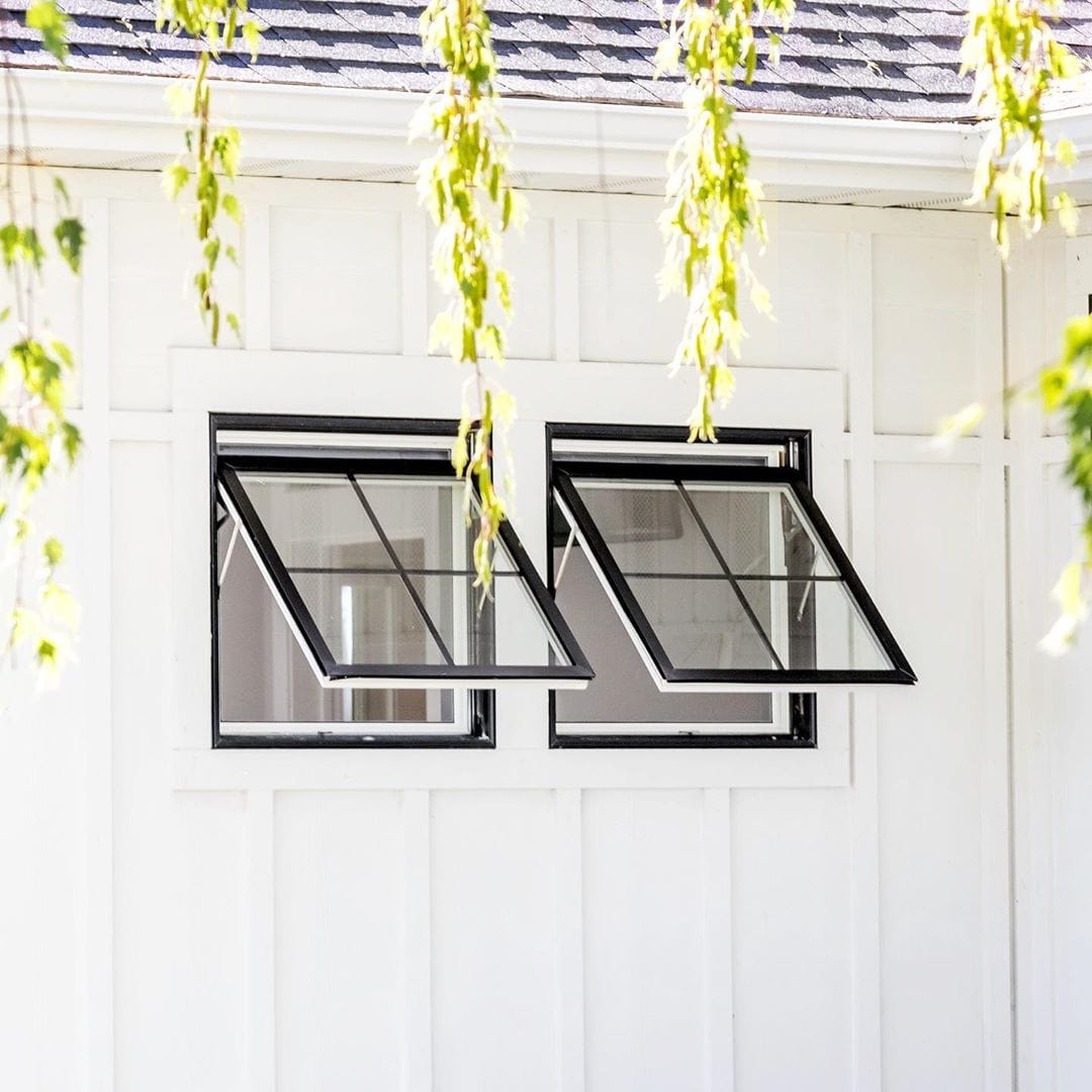 Awning Windows Provide Ventilation for Modern Farmhouse white siding with two black awning windows open and tree limbs hanging down