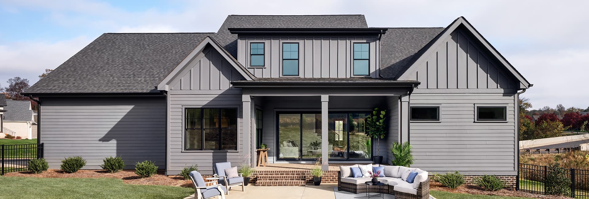 Modern gray farmhouse exterior with covered front porch, brick steps, patio seating and landscaped lawn