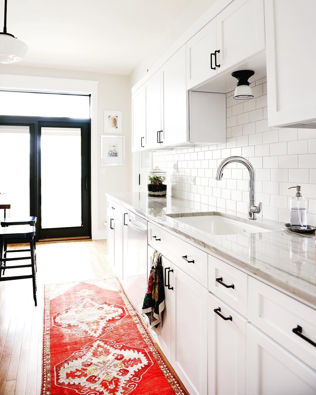 Black Patio Door Brings Contemporary Element to Kitchen contemporary white kitchen with red rug and black patio door