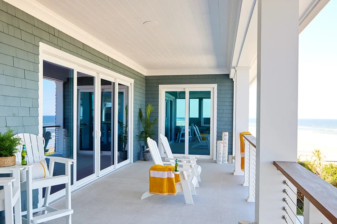 Beachfront patio with sliding hurricane doors, white chairs, and ocean view in the background.