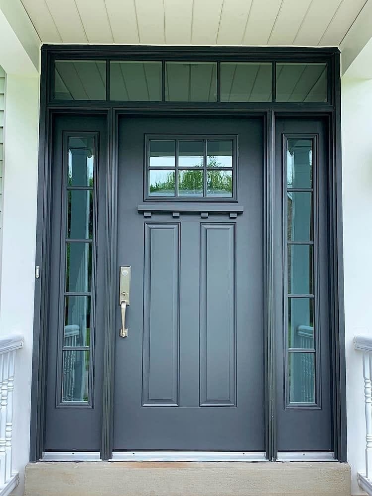 A fiberglass front door with glass and grilles is black and has a transom window and sidelights.