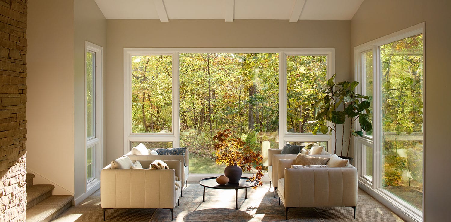 Replacement of large windows in a modern living room with beige sofas and a view of trees.