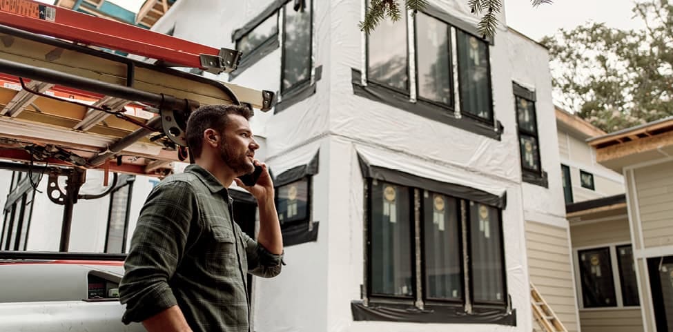 construction worker standing by a pickup on the phone outside a home under construction
