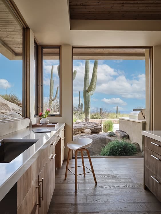 Tall cacti surrounded by rocks and green bushes sit outside a large southwestern-style kitchen.