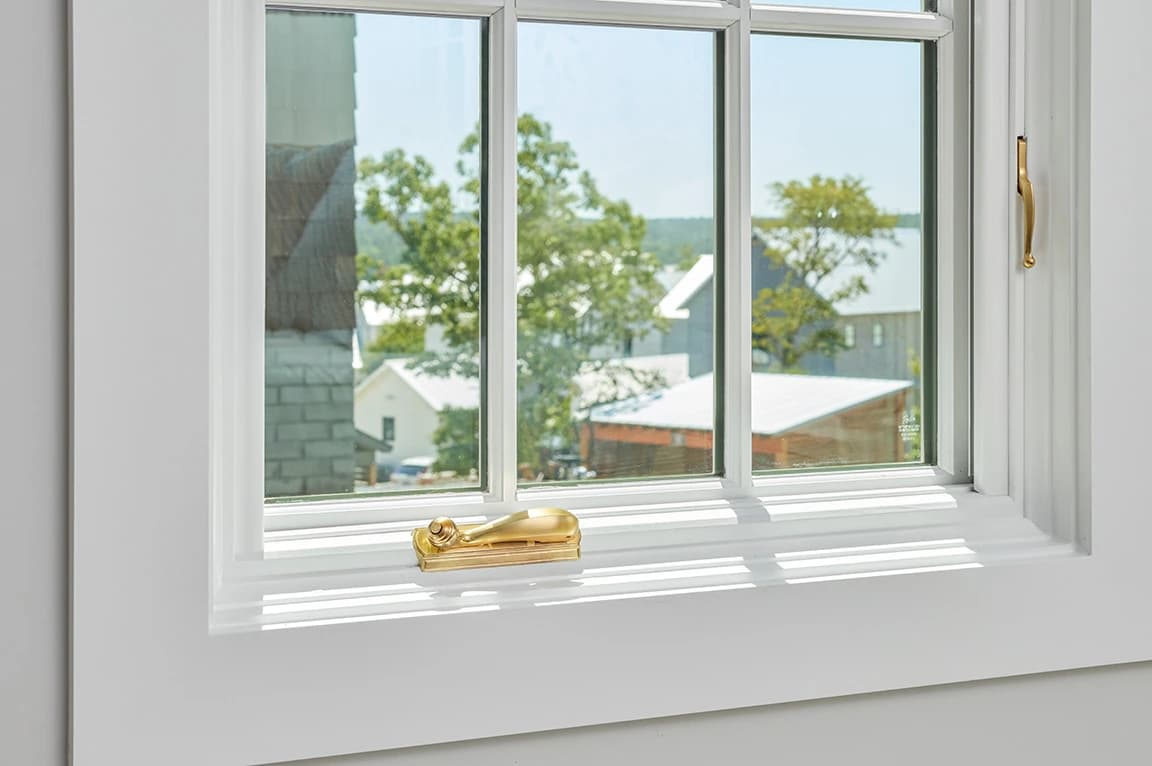 White-framed window with gold hardware showcasing parts of a window and an outdoor view.