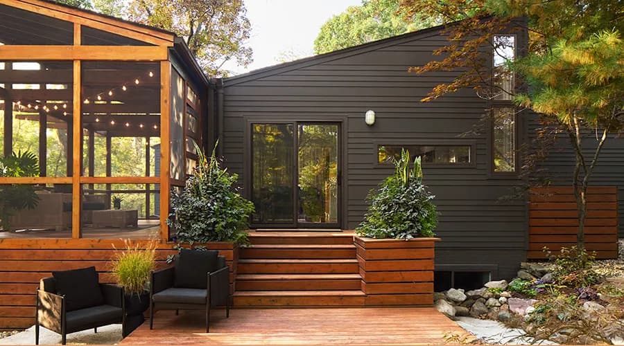 Black sliding door centered on a modern dark-sided house, with wooden steps and large planters leading up to the entrance.
