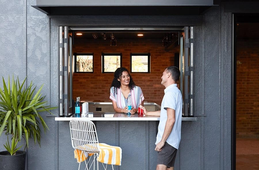 Two people standing around bar top walking between open pass-through windows