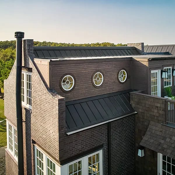 Three round windows with decorative grilles on a brown brick house exterior.