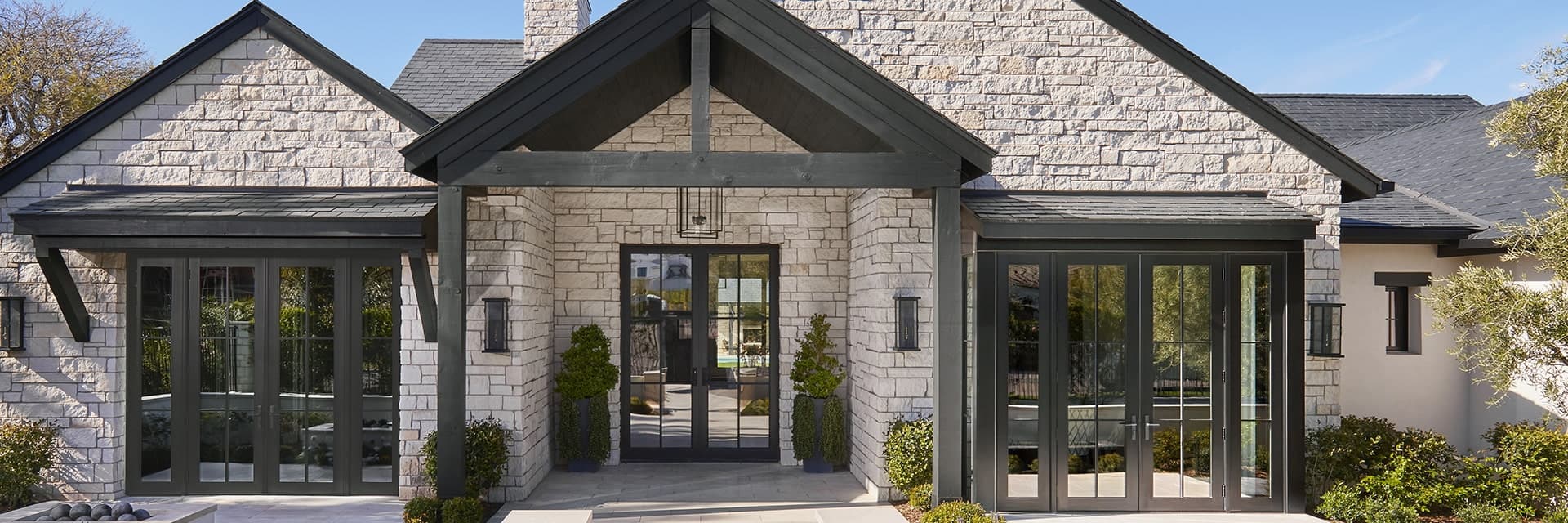 A home with a stone exterior with full glass front entry doors that sits underneath a black framed covering.