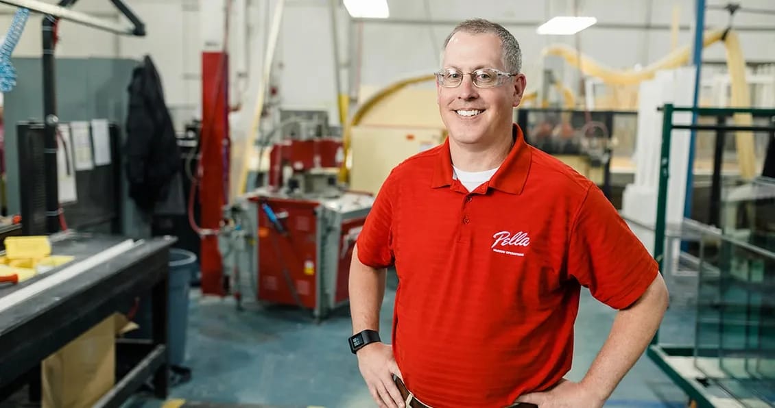 Man in a red shirt standing in a factory setting, highlighting careers in manufacturing.