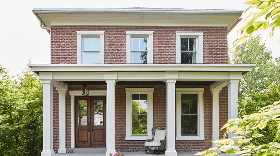 An old brick colonial home with white-trimmed windows and columns holding up the traditional front porch.