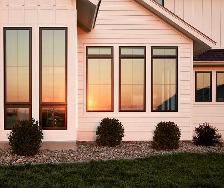 The sun is setting and casting an orange light on a white home with Pella Impervia black casement windows.