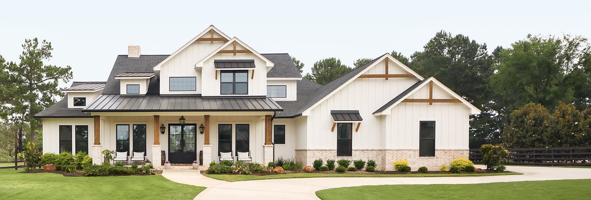 Large modern farmhouse with white board-and-batten siding, black metal roof, covered front porch and manicured lawn