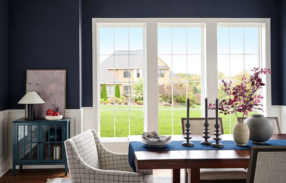 White vinyl windows on a dark blue wall looks out to a large green backyard and houses in the distance.