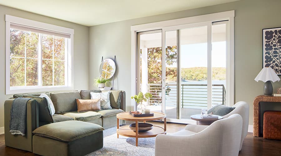 A white sliding patio door opens between a traditional living room and a patio that leads to a lake.
