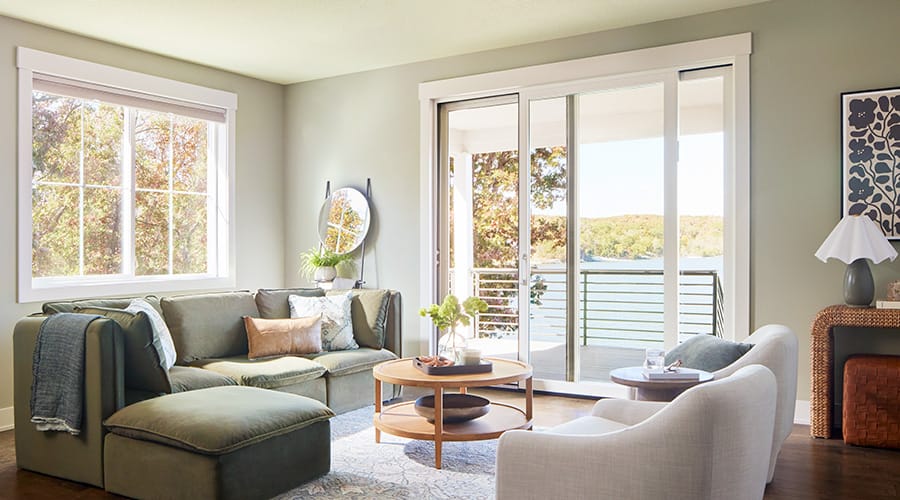 A white sliding patio door opens between a traditional living room and a patio that leads to a lake.