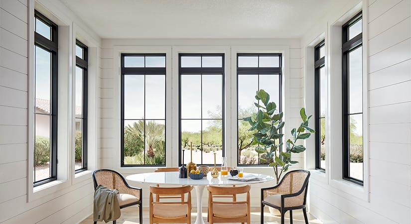 A dining room table in a room surrounded by black fiberglass windows.
