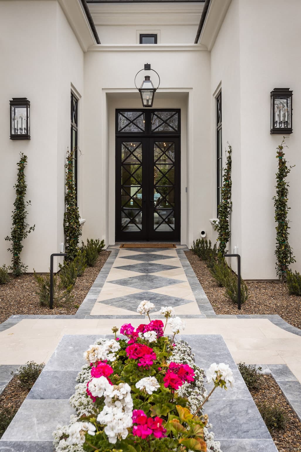 The exterior of a white stucco home features a traditional custom front door with a light hanging above it.