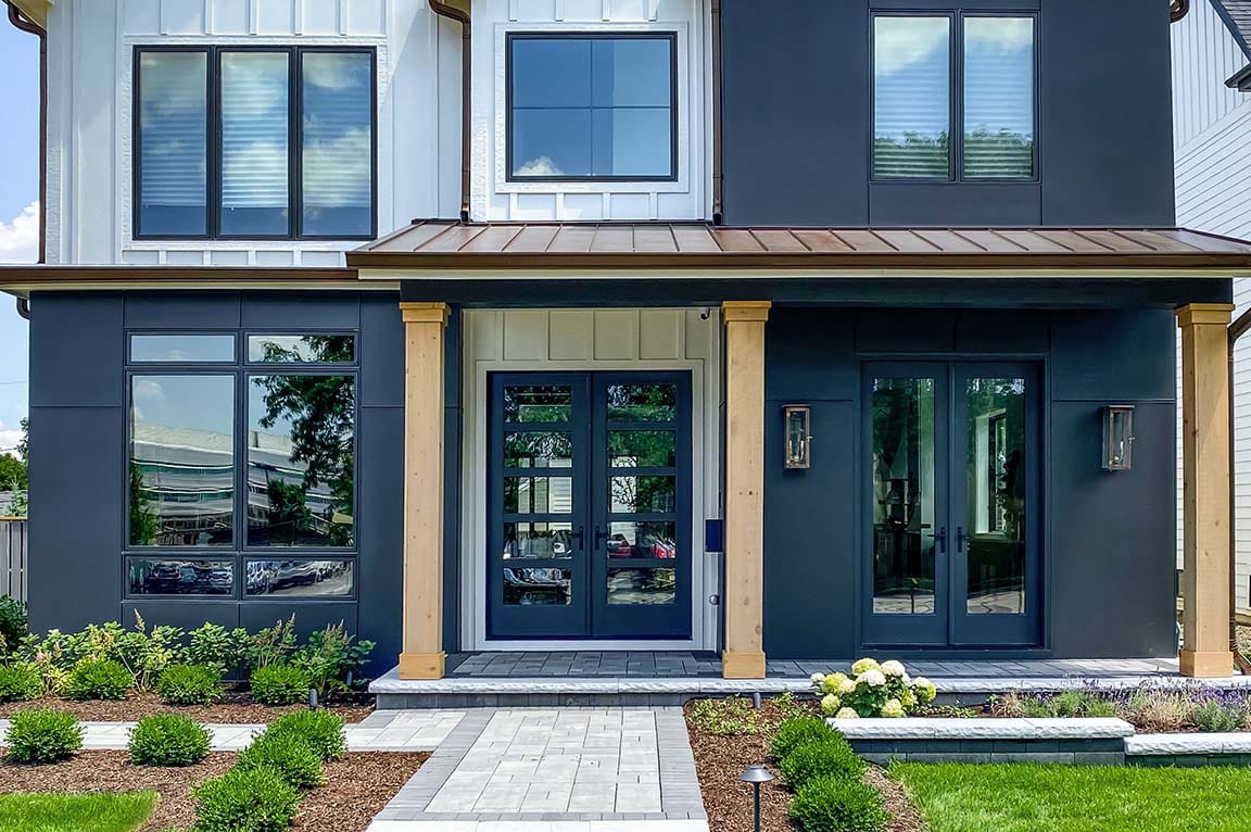 Modern farmhouse entry with black windows, glass front doors, and clean landscaping.