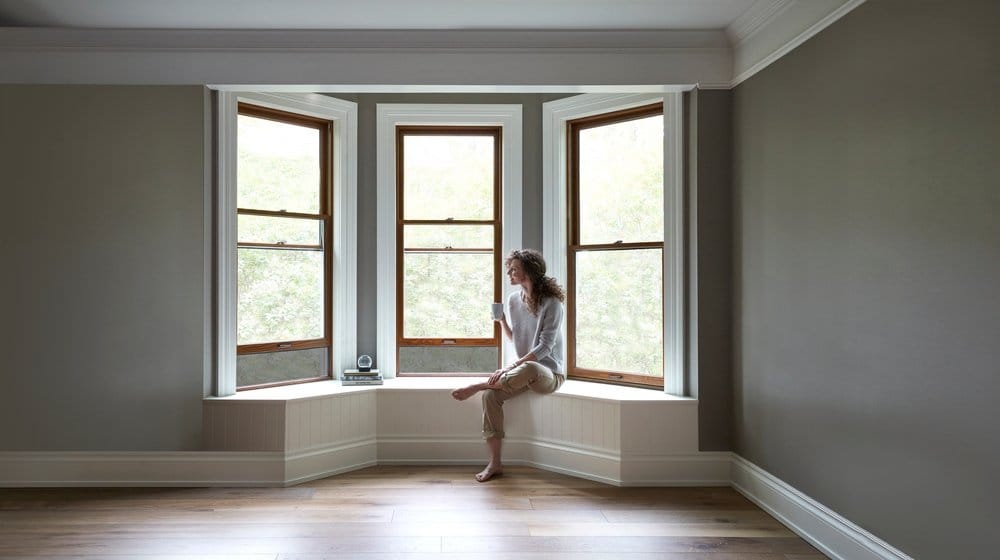 Custom Crafted Wood Bay Windows With Integrated Rolscreen® Wood stain bay windows with white trim and woman sitting on window seat