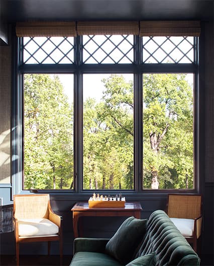 Elegant home office with dark walls and large Pella fixed grid windows overlooking green trees