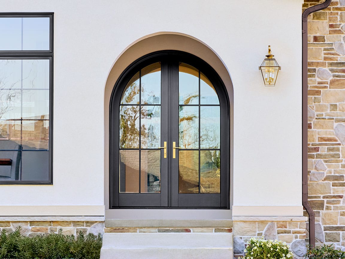 Arched black French entry door with glass panels on a stone-accented exterior.
