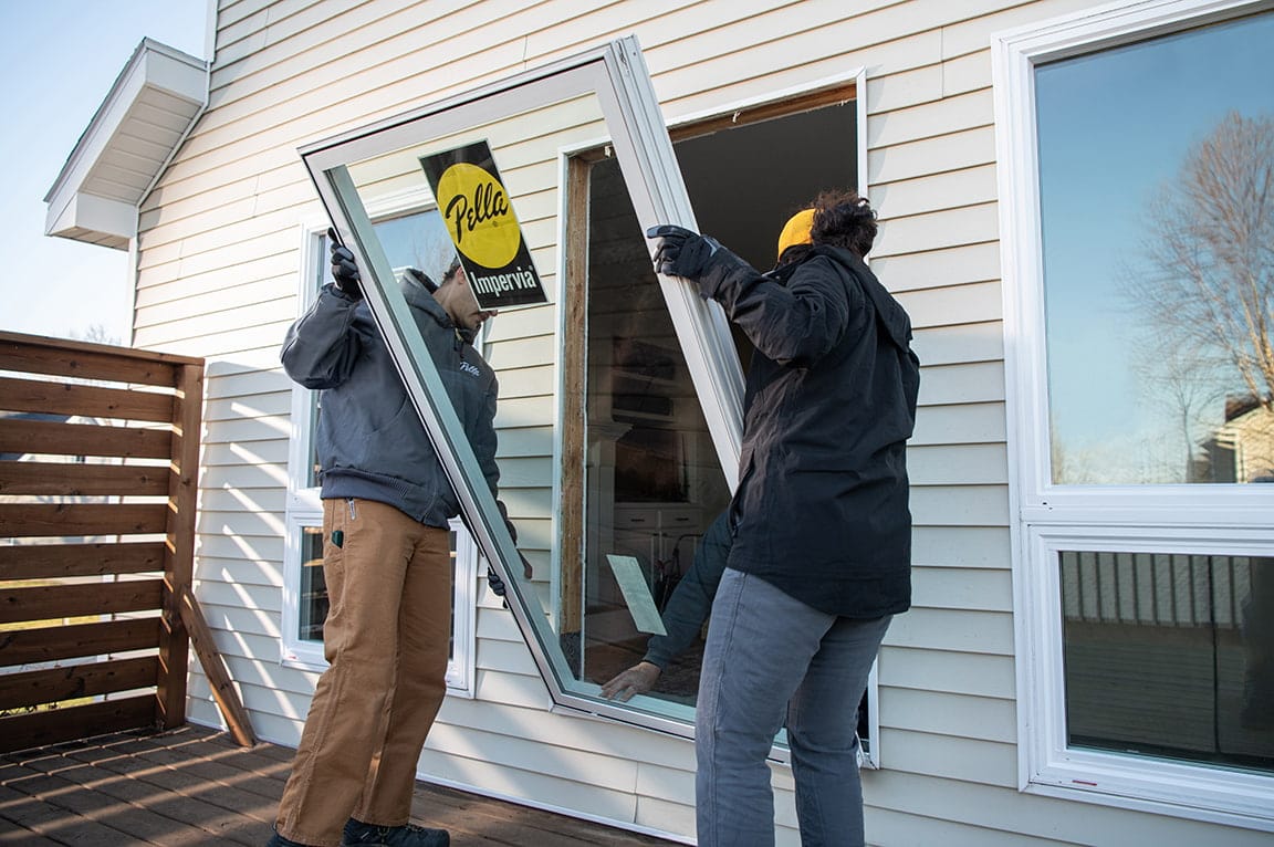 Two workers installing a Pella Impervia replacement window in a house, demonstrating replacing a replacement window.