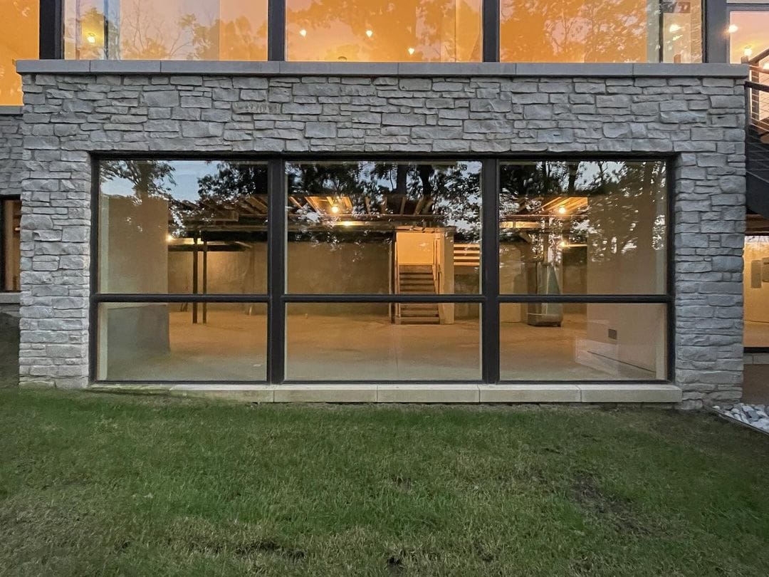 Black floor-to-ceiling windows look into the unfinished basement of a modern home.