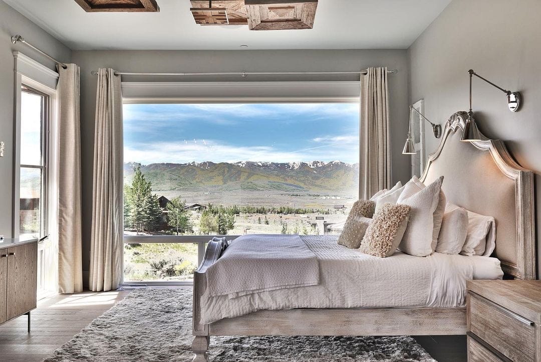 The back wall of a bedroom features a large picture window that frames the majestic mountain view beyond.