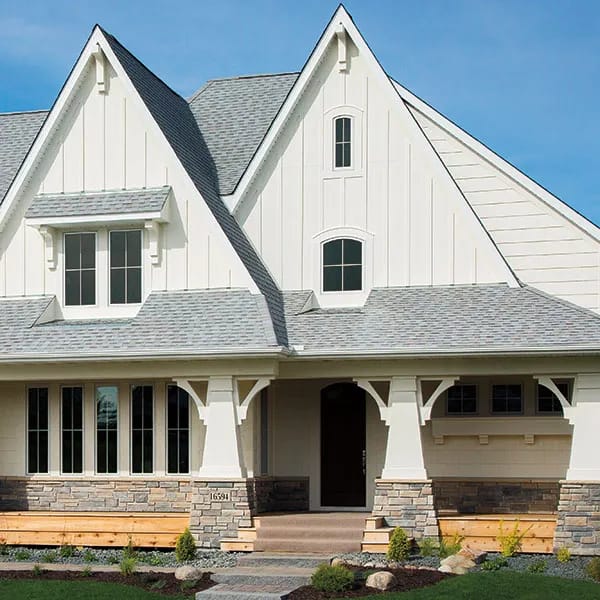 A white gable house with stone accents features multiple windows with vertical grilles on the front facade.