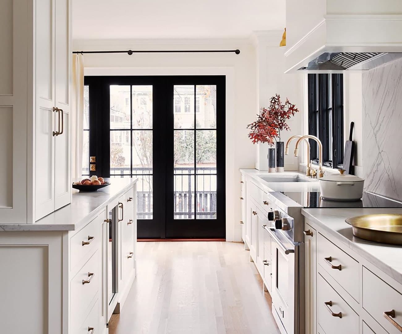 A white narrow kitchen has black hinged french patio doors on the far wall.