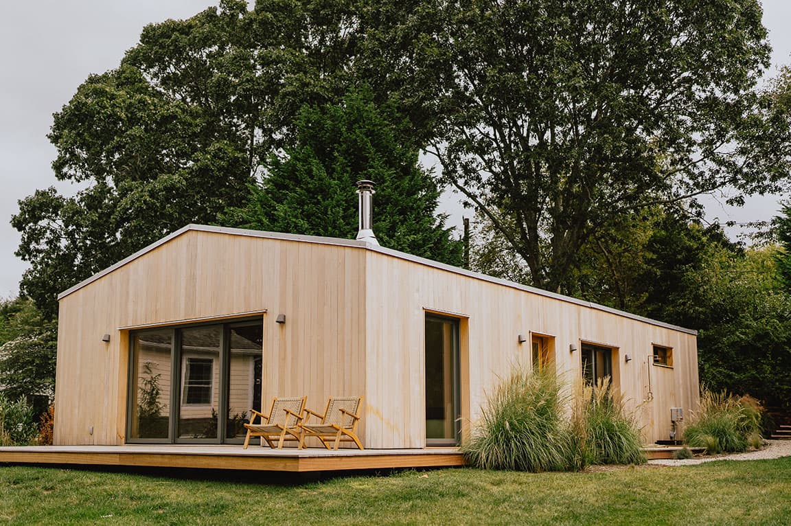 A modern wood-clad house with large energy efficient windows and sliding doors, surrounded by greenery.
