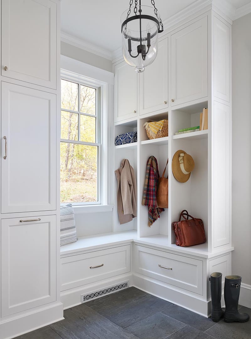 A white mudroom is brightened by a white double-hung window between the storage cabinets.