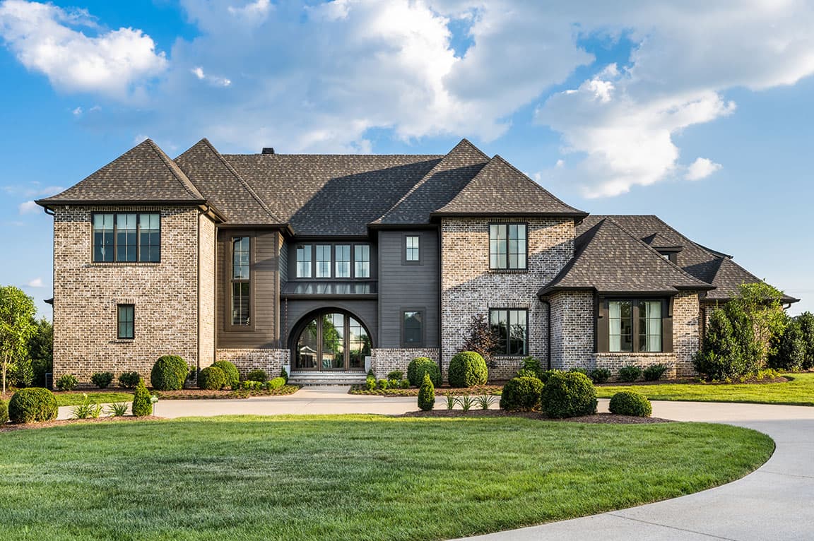 A modern home exterior featuring brown windows, stone and wood materials, and a landscaped garden.