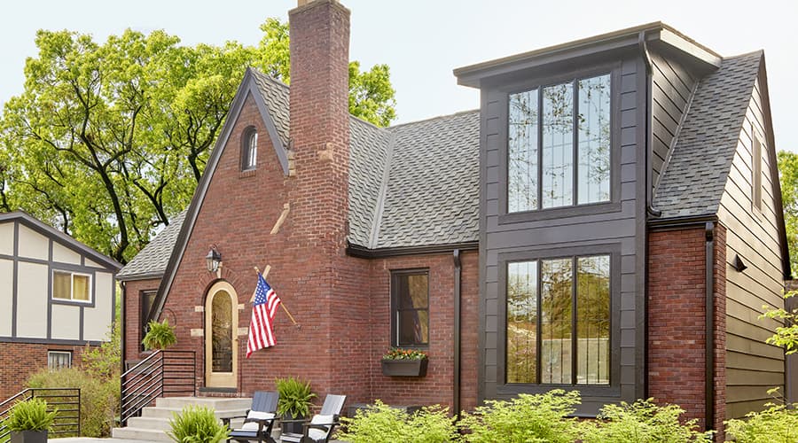 A brick home with a brick chimney has a newly renovated two story addition with mulled 3-wide casement windows.