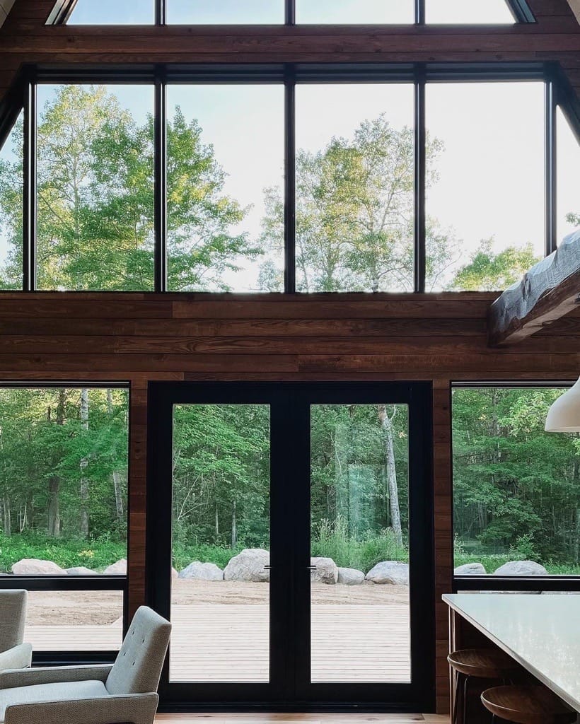 The wall of a living room features rustic modern French doors surrounded by windows.