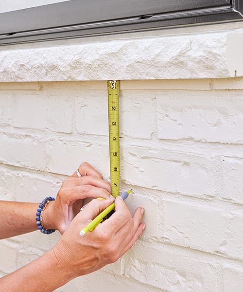 Using a tape measure to find the correct spot on an exterior wall and marking the spot with a pencil.