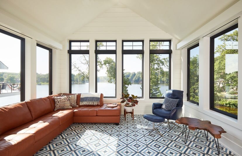 A sunroom with modern black windows has a leather sectional couch and blue chair.
