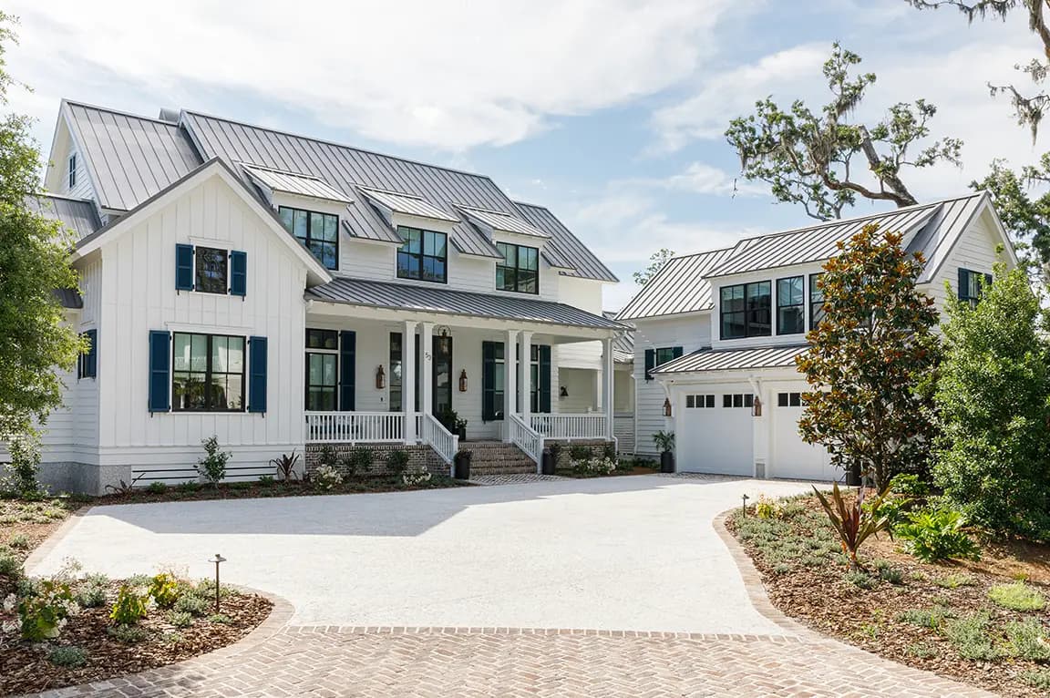 Modern white farmhouse-style two-story home with standing-seam metal roof, blue shutters, covered front porch, detached garage and landscaped driveway
